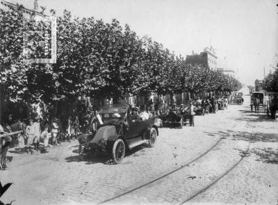 Automóviles desfilando por calle Sarmiento entre Mitre y Belgrano (Edificio de alto: Banco Provincia, edificio esquina al fondo con bandera: Banco Nación)