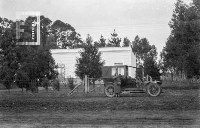 Dama y auto antiguo frente a casa de campo