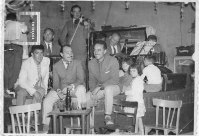 Grupo en torno a mesa de bar con orquesta al fondo