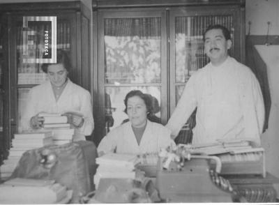 Un señor y dos damas de guardapolvos junto a escritorio