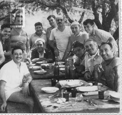 Grupo  en torno a mesa de asado bajo árboles