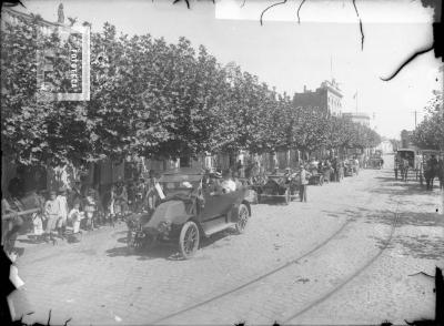 Automóviles desfilando por calle Sarmiento entre Mitre y Belgrano (Edificio de alto: Banco Provincia, edificio esquina al fondo con bandera: Banco Nación)