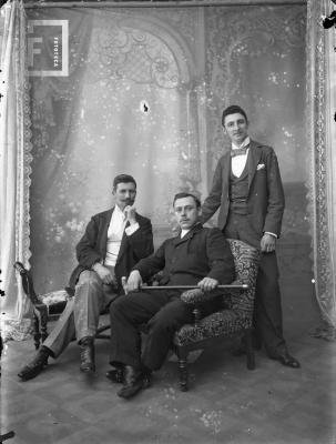 Carlos L. Bustos parado y dos hombres sentados