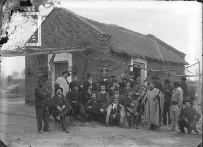 Grupo con orquesta frente a rancho. Entre ellos Mario Castellazzi (sobresaliendo atrás justo en esquina rancho) y el violoncelista Enrique Bomón, con su instrumento