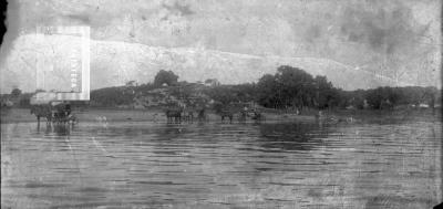 Pequeña placa, carros en río y ranchos en barranca al fondo