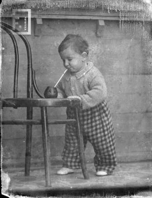 Niño tomando mate apoyado en silla